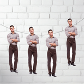 Four identical men standing against a white brick wall.